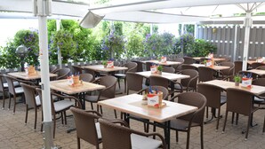 Un café al aire libre con sillas y mesas de mimbre, algunas con artículos de la marca 'SPRITE'.
