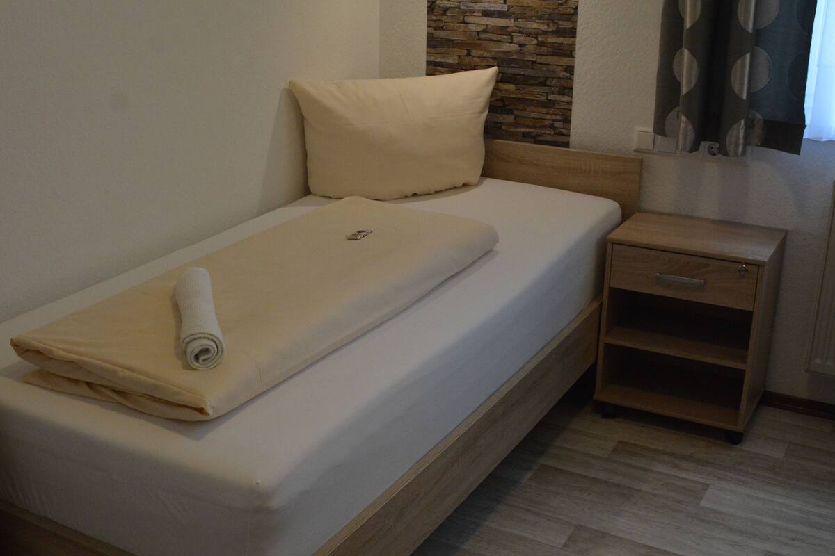 Una cama individual con cabecera de madera, una mesita de noche pequeña y una pared con detalles de piedra.