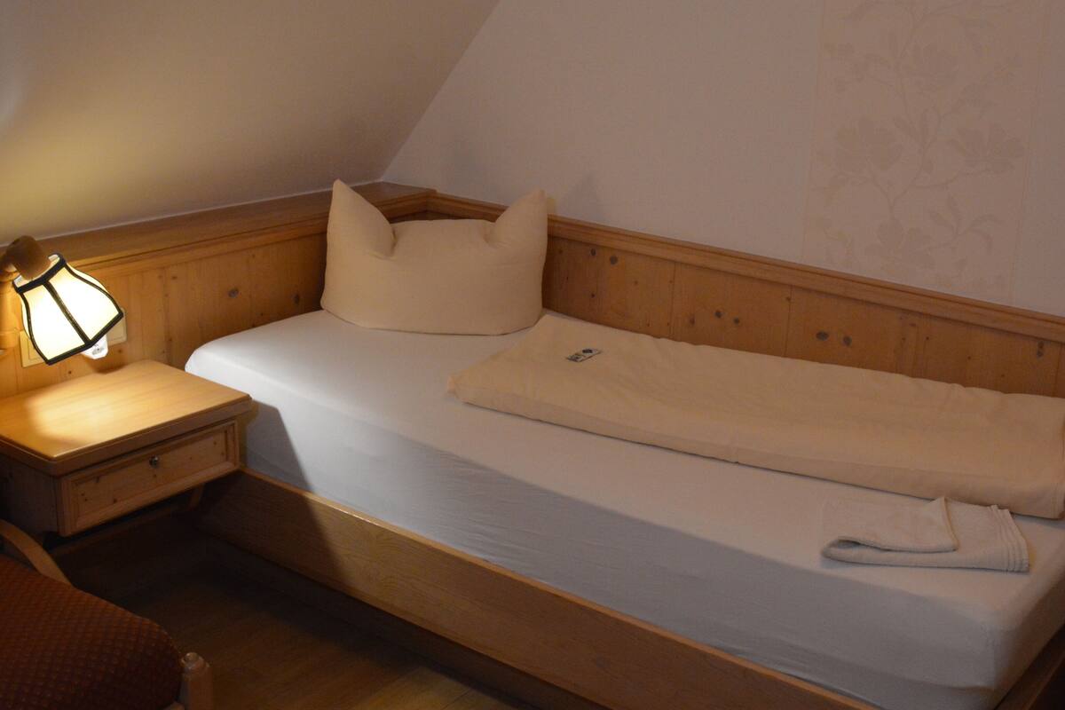Una cama individual con cabecera de madera, una mesita de noche con lámpara y una pared con estampado floral.