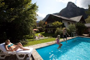 A swimming pool with people around it, a house, and mountains in the background. - DAS Posch Hotel (Oberammergau)