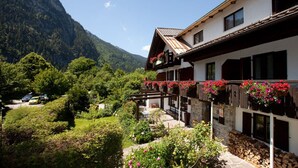 A mountain lodge with a balcony adorned with flowers, surrounded by lush greenery and a mountain backdrop. - DAS Posch Hotel (Oberammergau)