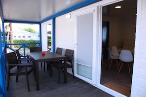 Un espace extérieur abrité, doté d’une table et de chaises, une porte coulissante donnant accès à un espace intérieur, et une vue sur un bâtiment en arrière-plan.
