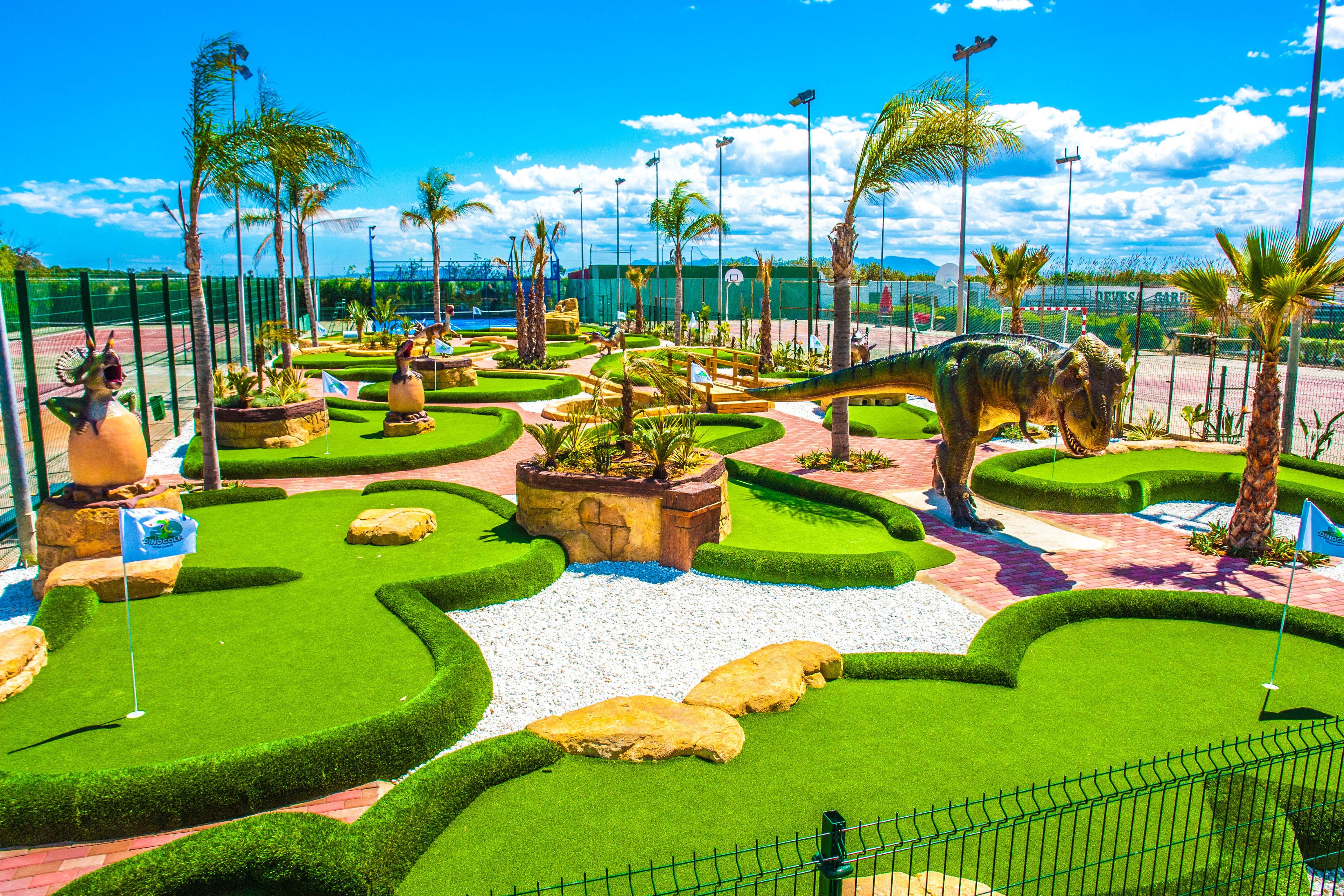 Un jardín bien cuidado con varias esculturas, un camino sinuoso y una gran estatua de dinosaurio.