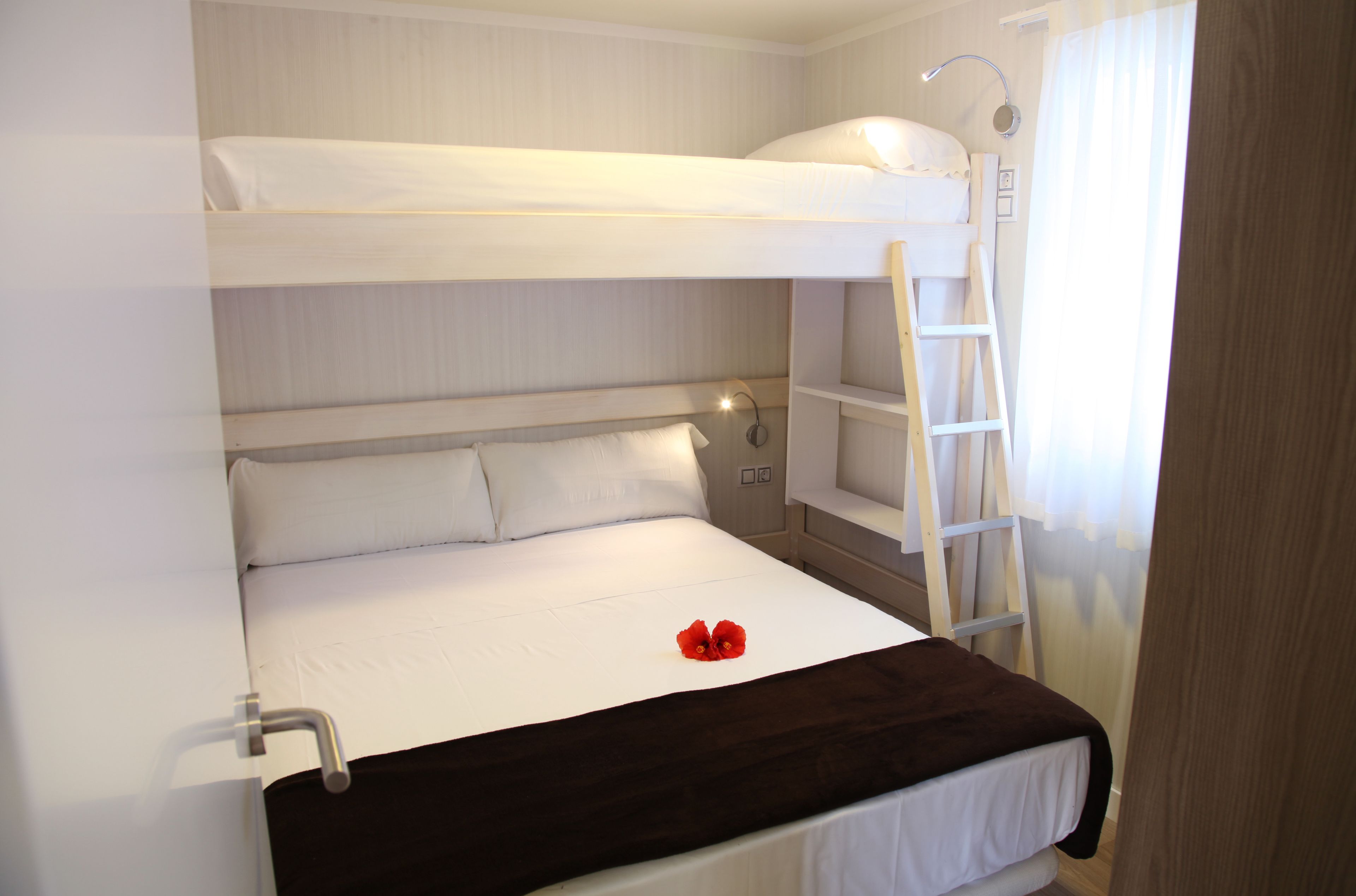 A bunk bed with a ladder, a bedside table, and a red flower decoration.