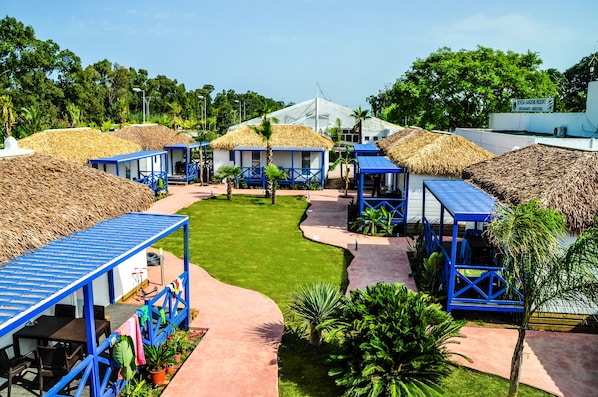 Un complexe hôtelier doté de bungalows aux toits de chaume, d’une pelouse centrale et d’un bâtiment blanc avec une enseigne.