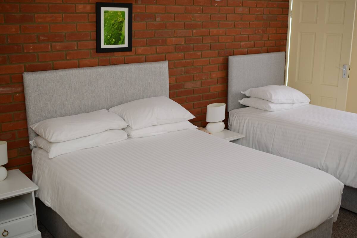A hotel room with two beds, a brick wall, a framed picture, and a door.