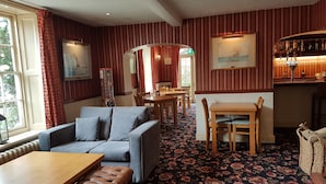 A cozy room with a sofa, a wooden table, a patterned carpet, and a bar area with bottles. - Park Hill Hotel (Lowestoft)