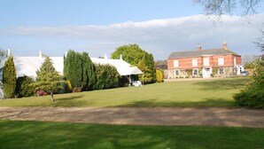 A large, open grassy area with a white tent and a red brick building in the background. - Park Hill Hotel (Lowestoft)