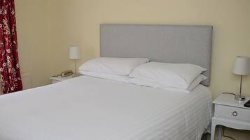 Una cama bien hecha con sábanas blancas, dos mesitas de noche con lámparas y una cortina roja con estampado floral.
