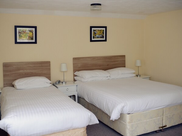 Habitación de hotel con dos camas, cada una con ropa blanca y cabeceros. Se observan mesitas de noche con lámparas y un pequeño reloj.