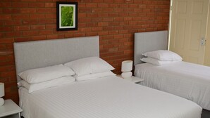 A hotel room with two single beds, a brick wall, a framed picture, and a door. - Park Hill Hotel (Lowestoft)
