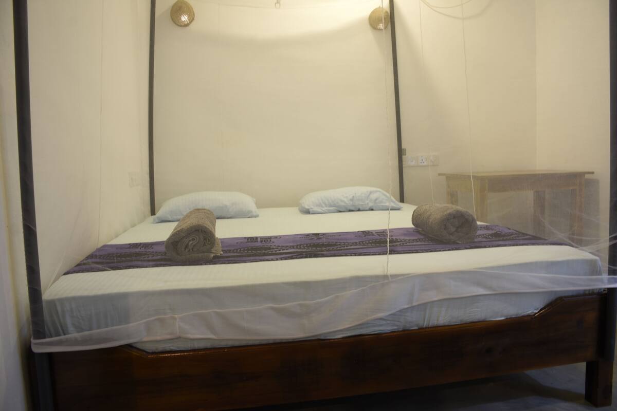 Ein Einzelbett mit Holzrahmen, weißen Laken und zwei aufgerollten Handtüchern.