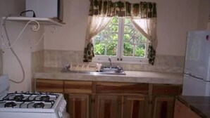 A kitchen with a gas stove, wooden cabinets, a window with curtains, and a refrigerator. - Symphony Resort (Discovery Bay)