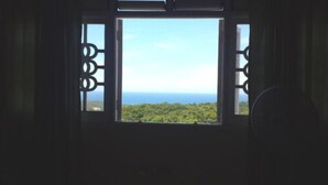 A window with a view of a green landscape and the ocean. - Symphony Resort (Discovery Bay)