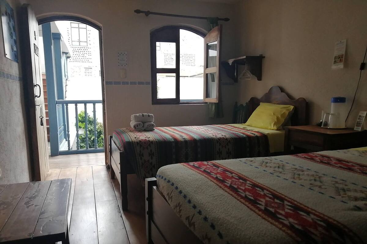 A room with two beds, a wooden table, and a balcony.