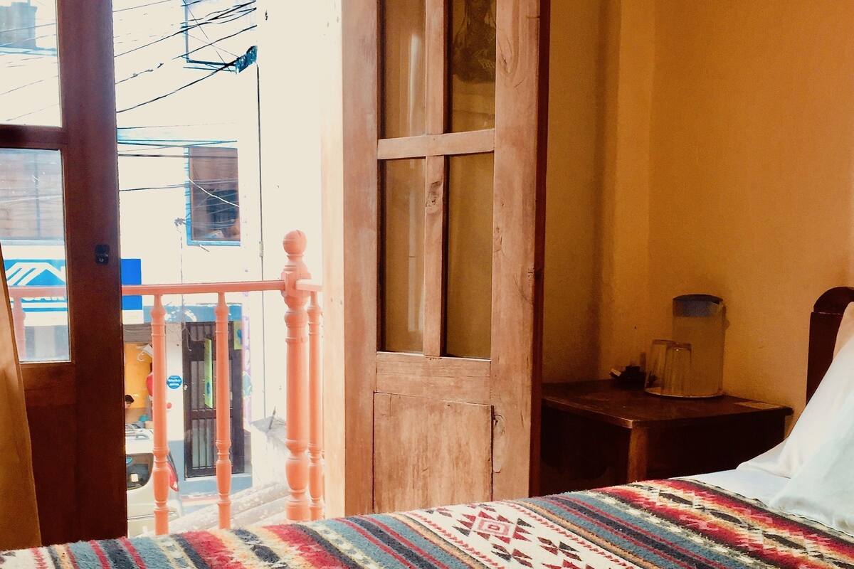 A room with a bed, a wooden door, and a view of the outside.