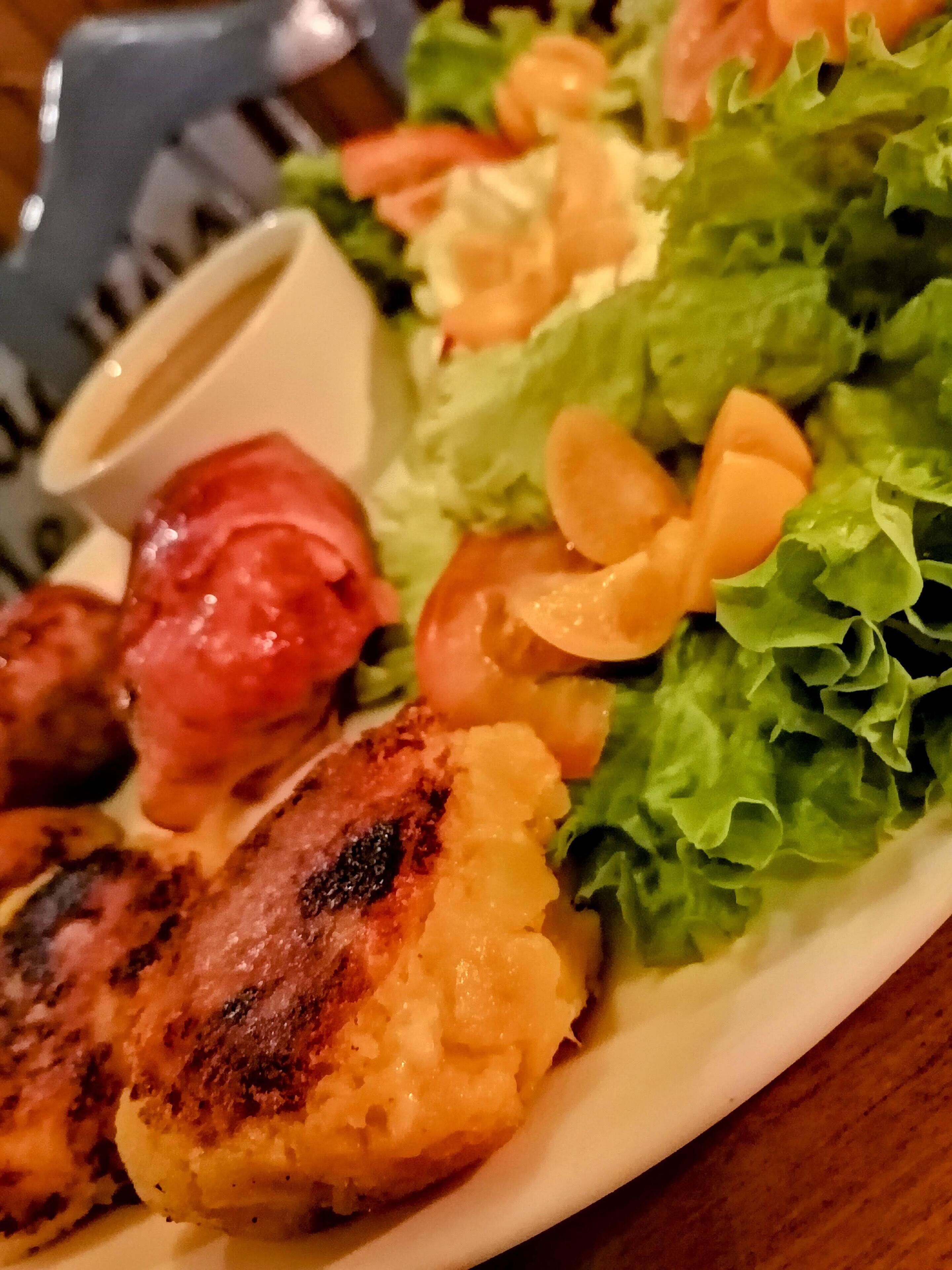 A plate of food with grilled meat, vegetables, and a small bowl of sauce.