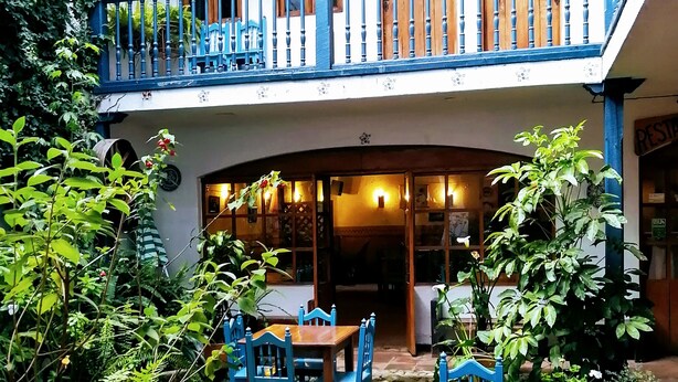 A courtyard with a two-story building, outdoor seating area with tables and chairs, and a small water feature. - Hotel Doña Esther (Otavalo)