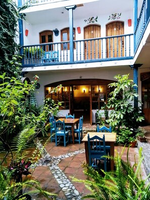 A courtyard with a two-story building, outdoor seating area with tables and chairs, and a small water feature. - Hotel Doña Esther (Otavalo)