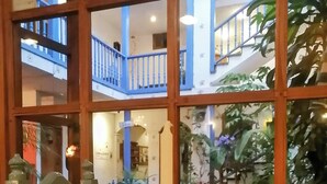 A dining area with a table set for two, a candle centerpiece, and a view of a multi-level building with balconies. - Hotel Doña Esther (Otavalo)