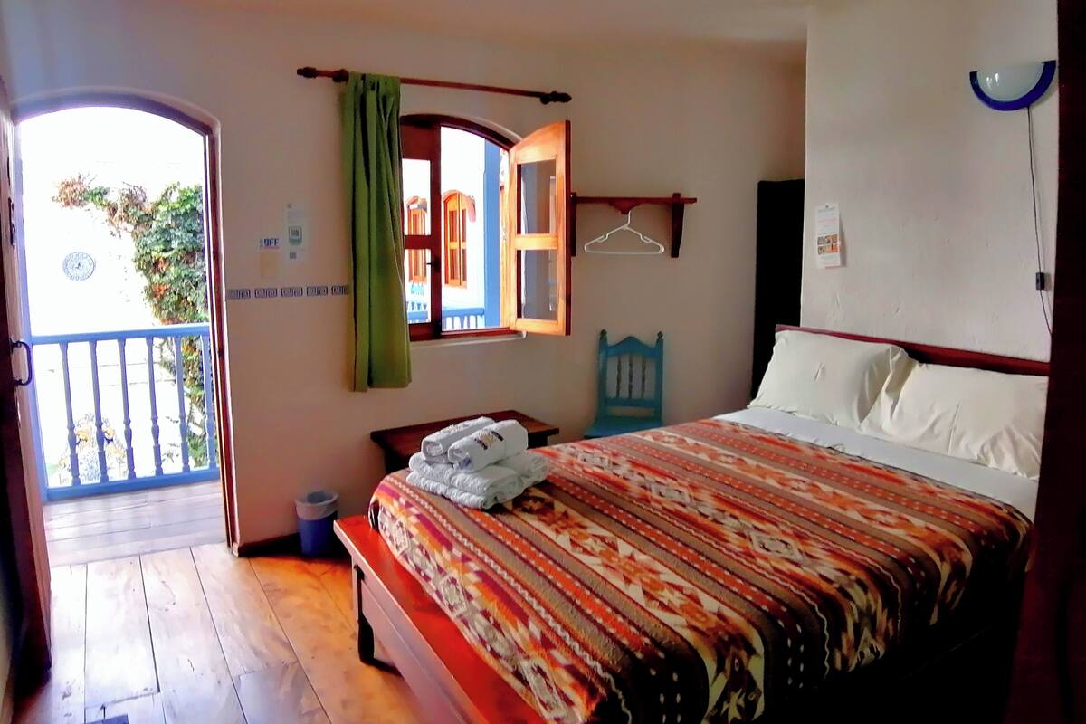 A bedroom with a bed, a window with a view, a hanging light fixture, and a small table.