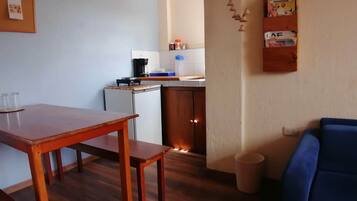 Een knus woongedeelte met een houten eettafel, een kitchenette met een koffiezetapparaat en een blauwe bank.