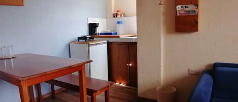 A compact living space with a wooden dining table, a kitchenette with a coffee maker, and a blue couch.