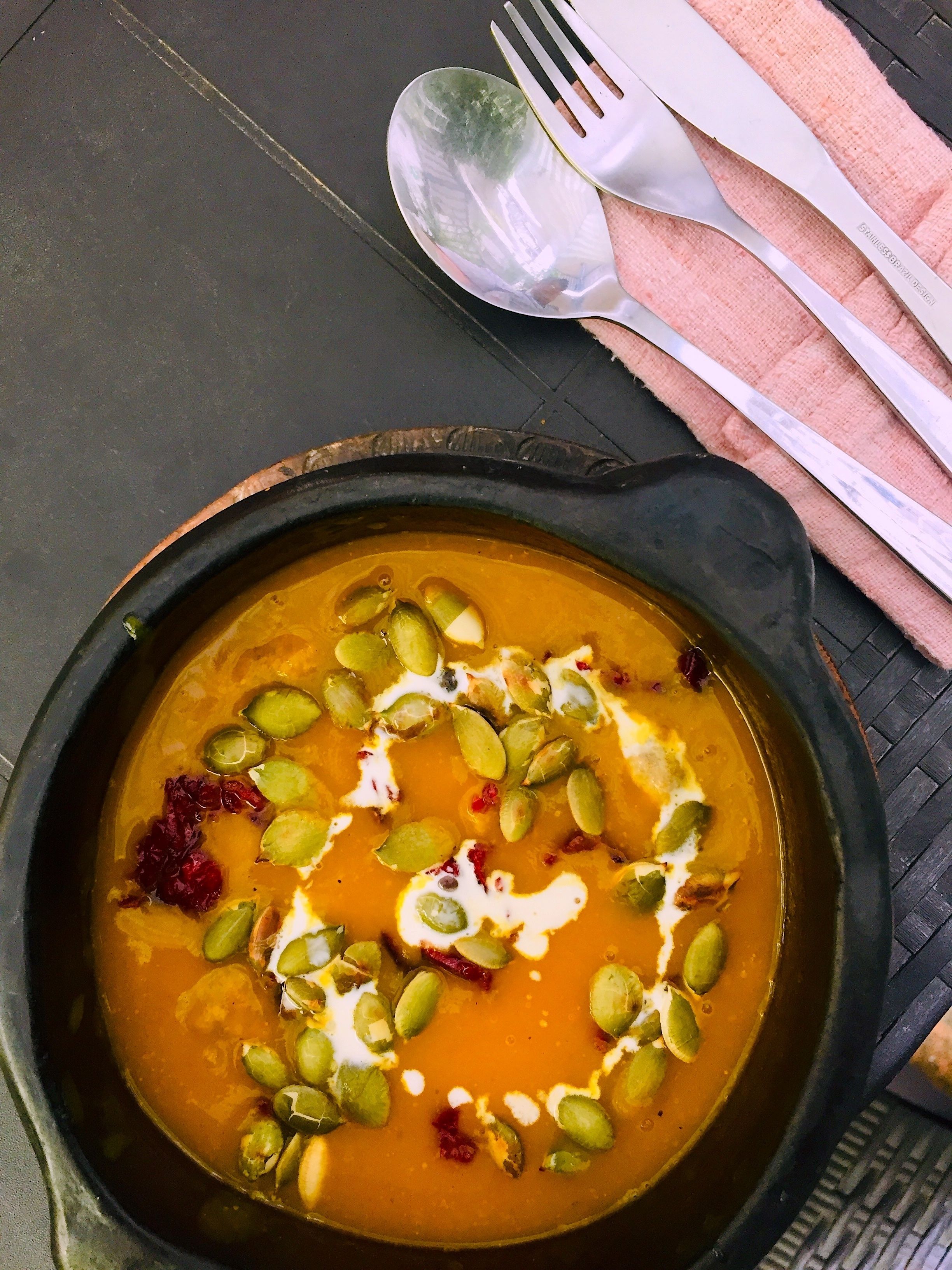 A bowl of soup with pumpkin seeds and a dollop of cream on a black plate.