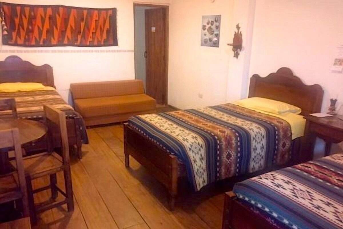 A room with two beds, a sofa, a wooden table, and a patterned rug.
