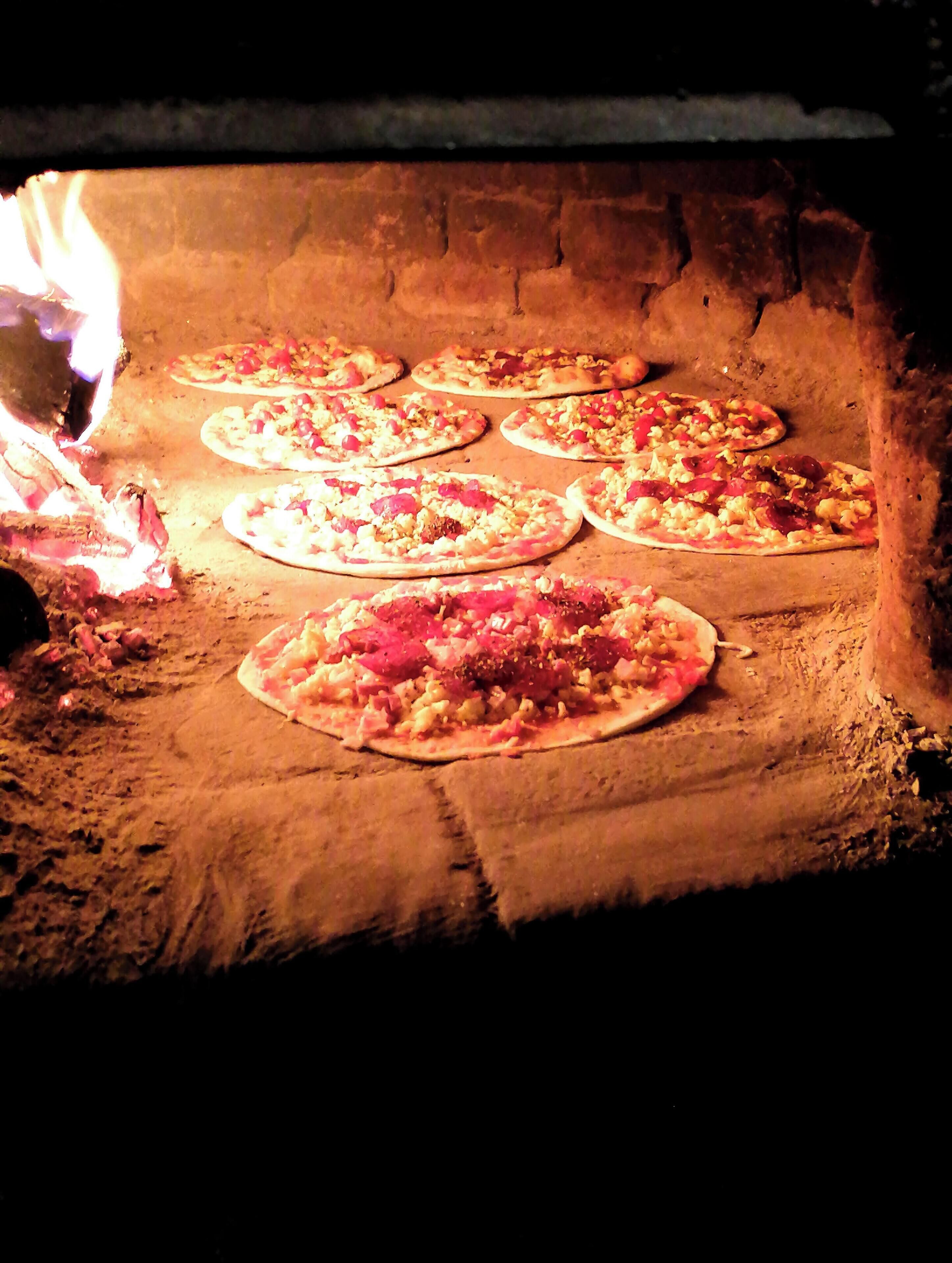 Pizzas assando em forno de tijolos.