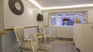A room with a clock, two chairs, a small table with a candle, a window with flowers, and a radiator. - Zeynep Hatun Otel (Biga)