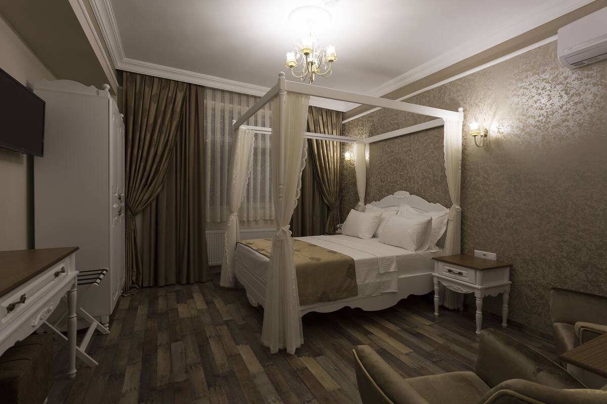 Una cama con dosel, una mesita de noche, una silla y un televisor en la pared.