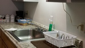 A kitchen with wooden cabinets, a granite countertop, a stainless steel sink, and a coffee maker. - Becket Motel (Becket)