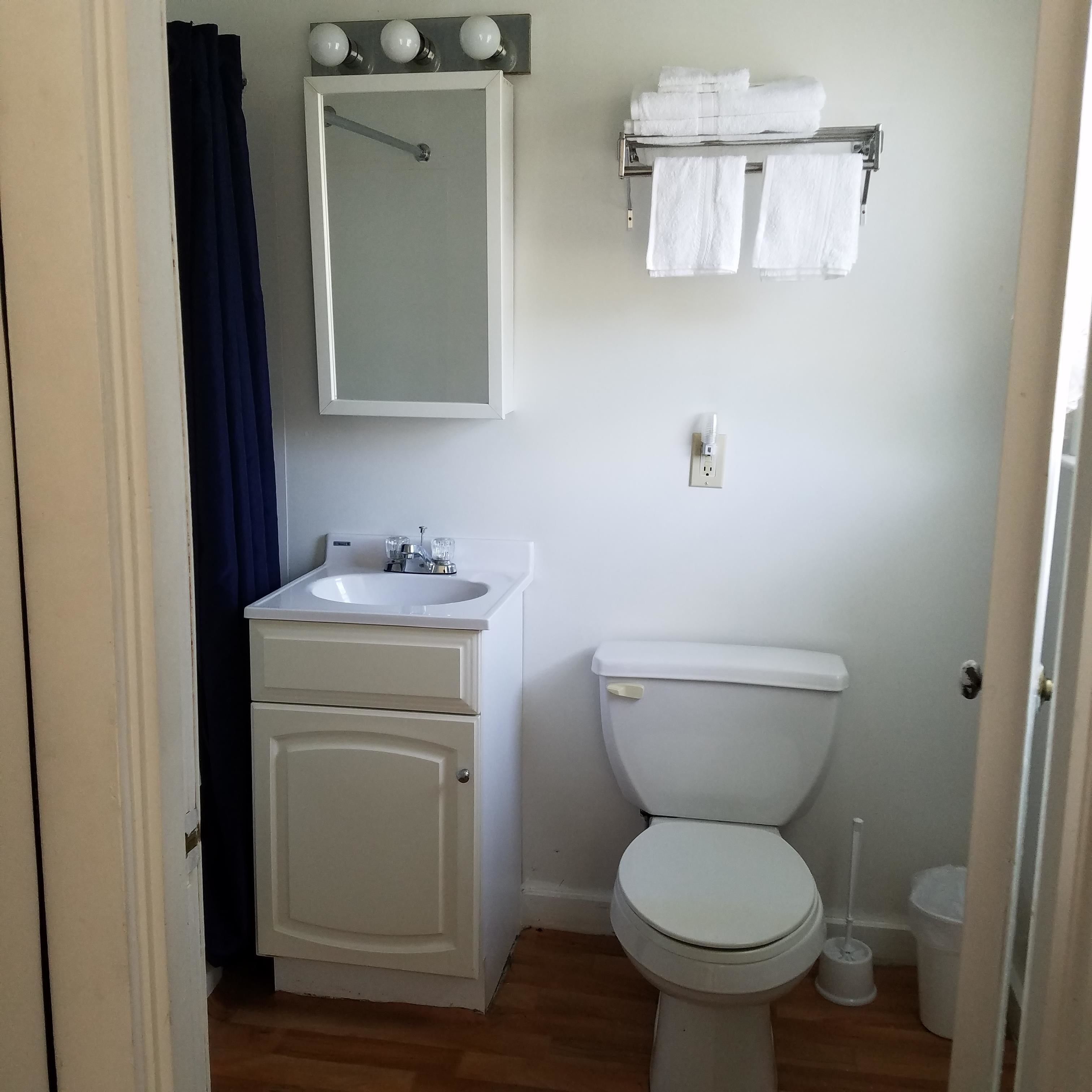 A bathroom with a white sink, mirror, and toilet. There is a towel rack with towels above the toilet.