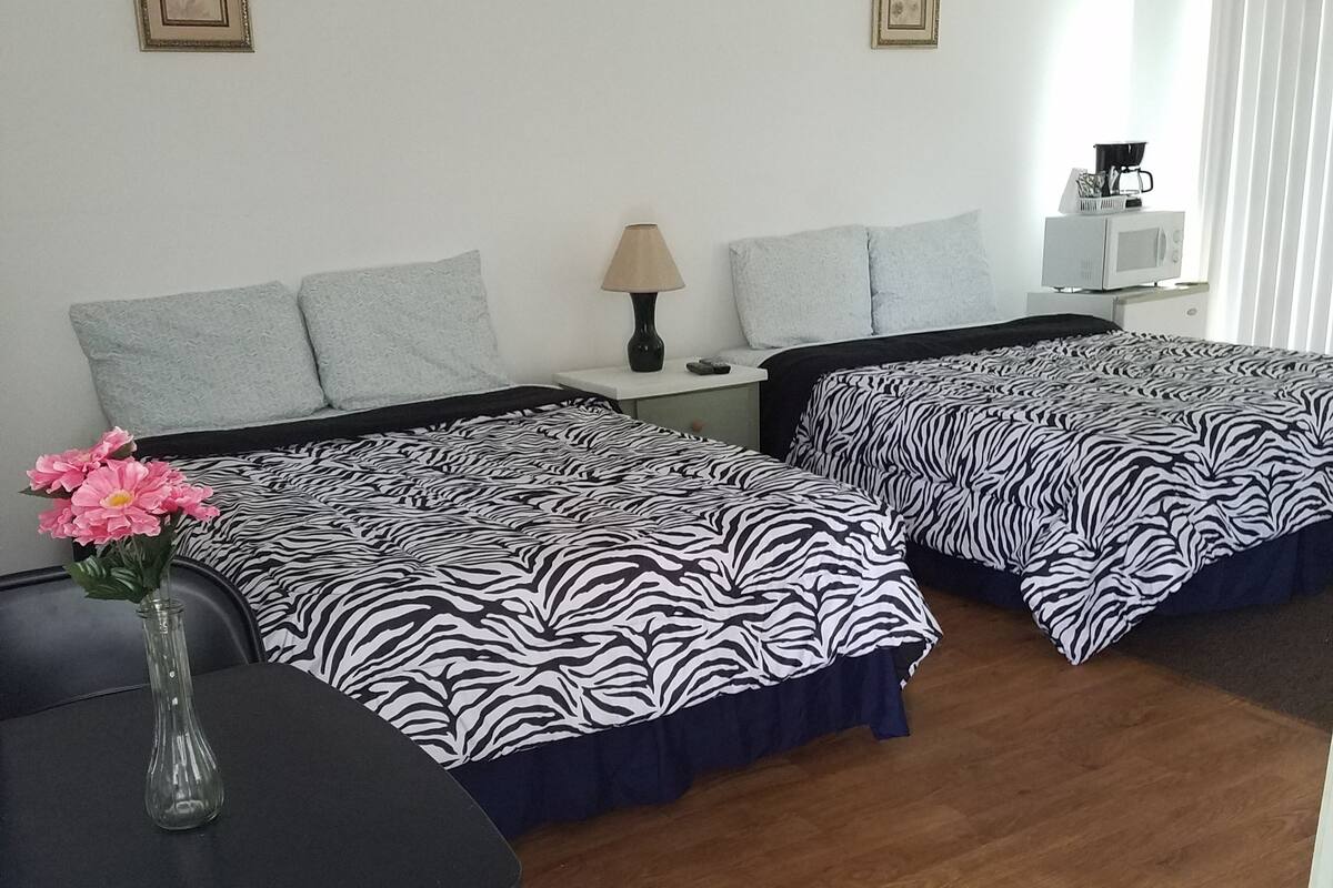 Habitación de hotel con dos camas, una mesita con un florero, una lámpara y un microondas sobre la encimera.
