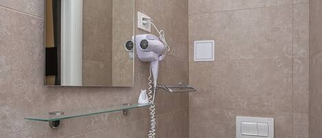 A modern bathroom with a large mirror, a hairdryer mounted on the wall, a white sink, and a toilet.