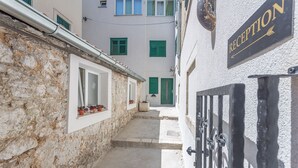 Un estrecho callejón con un letrero de recepción, paredes de piedra y contraventanas verdes en las ventanas.