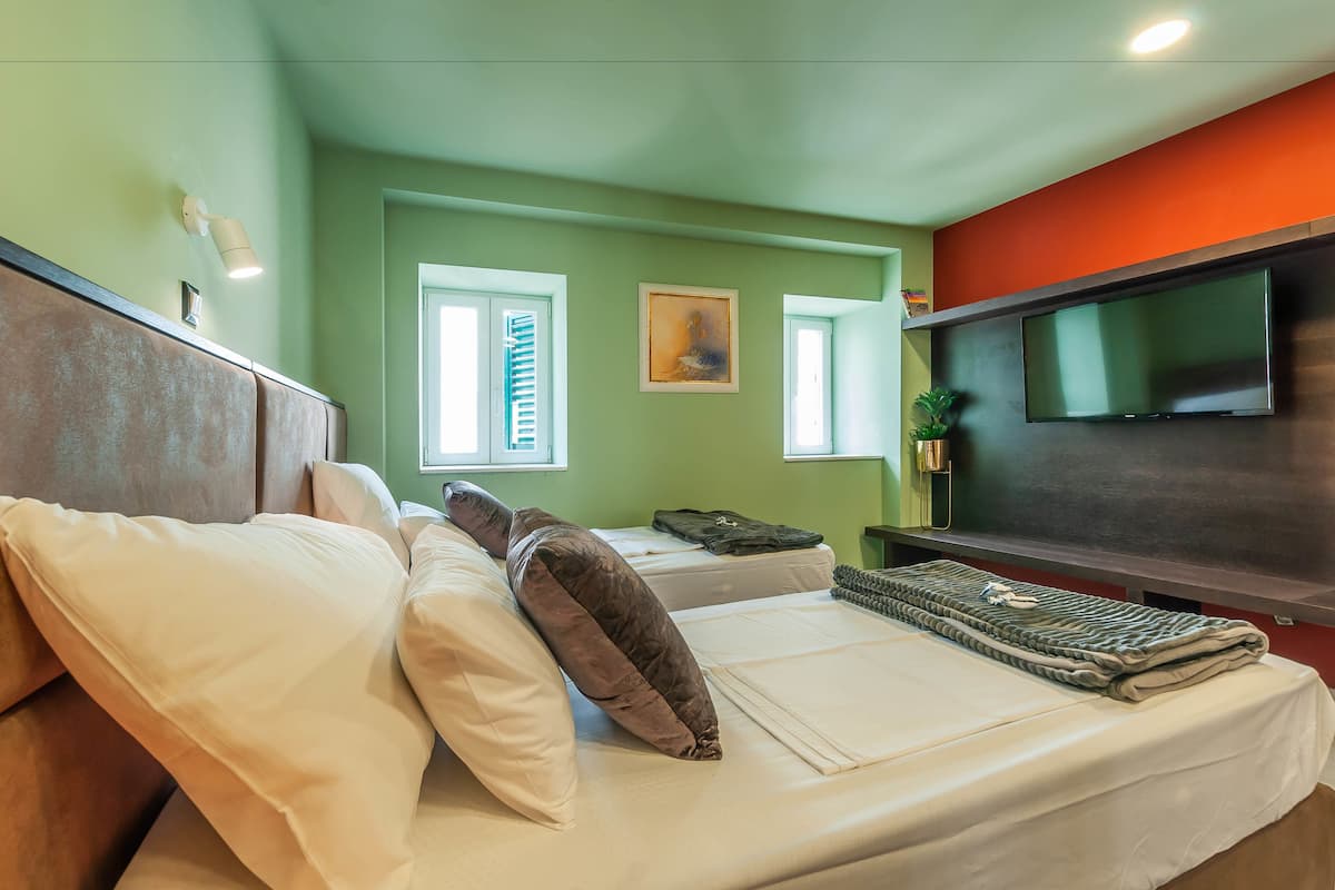 Quarto de hotel com duas camas, televisão de tela plana e janela com persianas.
