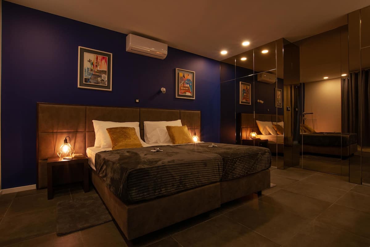 Quarto moderno com uma cama grande, duas mesas de cabeceira com luminárias, ar condicionado fixado na parede e obras de arte emolduradas.