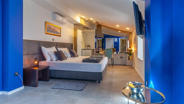 Una habitación de hotel moderna con una cama grande, mesitas de noche, un televisor de pantalla plana y una pequeña zona de kitchenette.