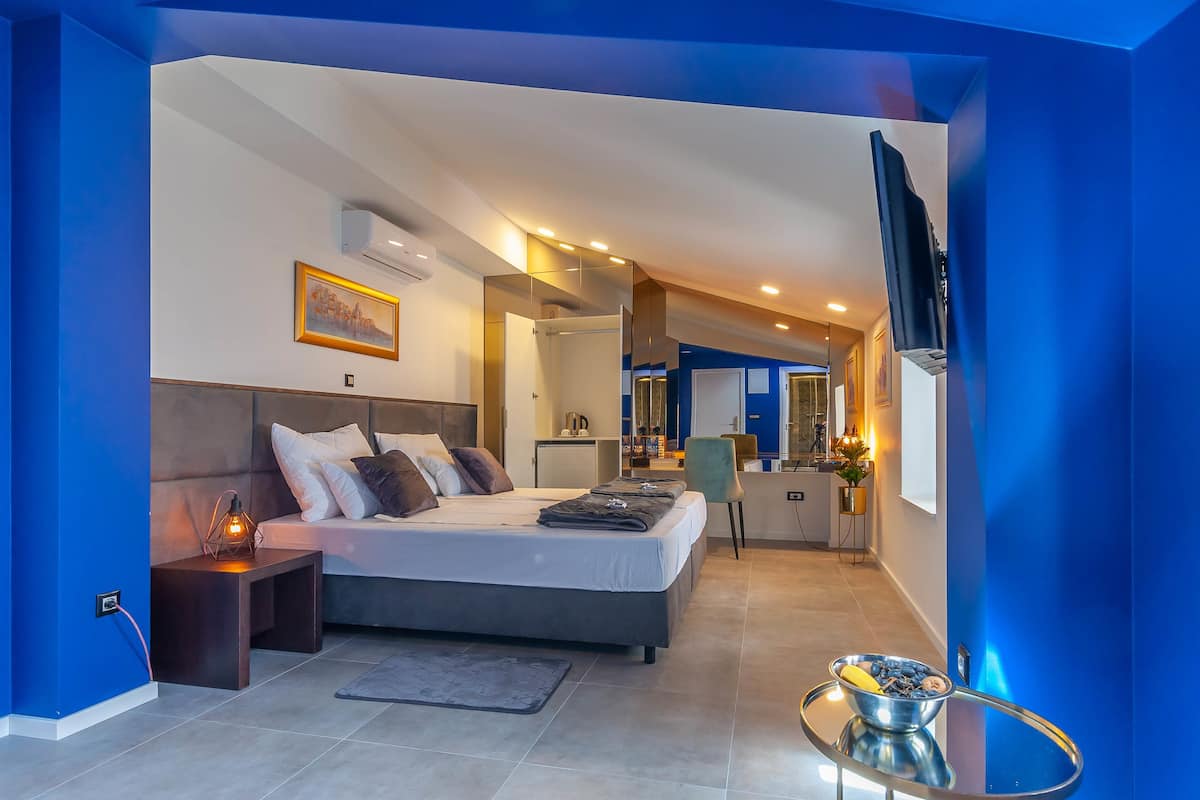Quarto de hotel moderno com uma cama grande, mesas de cabeceira, uma TV de tela plana e uma pequena cozinha.
