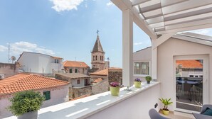 Un balcón con plantas en macetas, una silla y vistas a un edificio histórico con una torre.