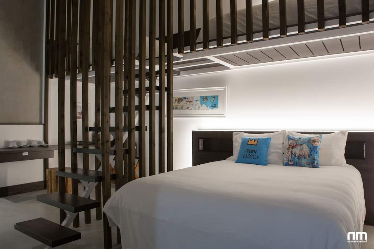 A modern bedroom with a large bed, a wooden partition, and a small desk with a chair.