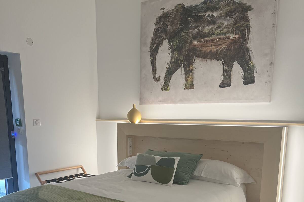 A neatly made bed with a green blanket, a headboard, and a framed elephant artwork above it.