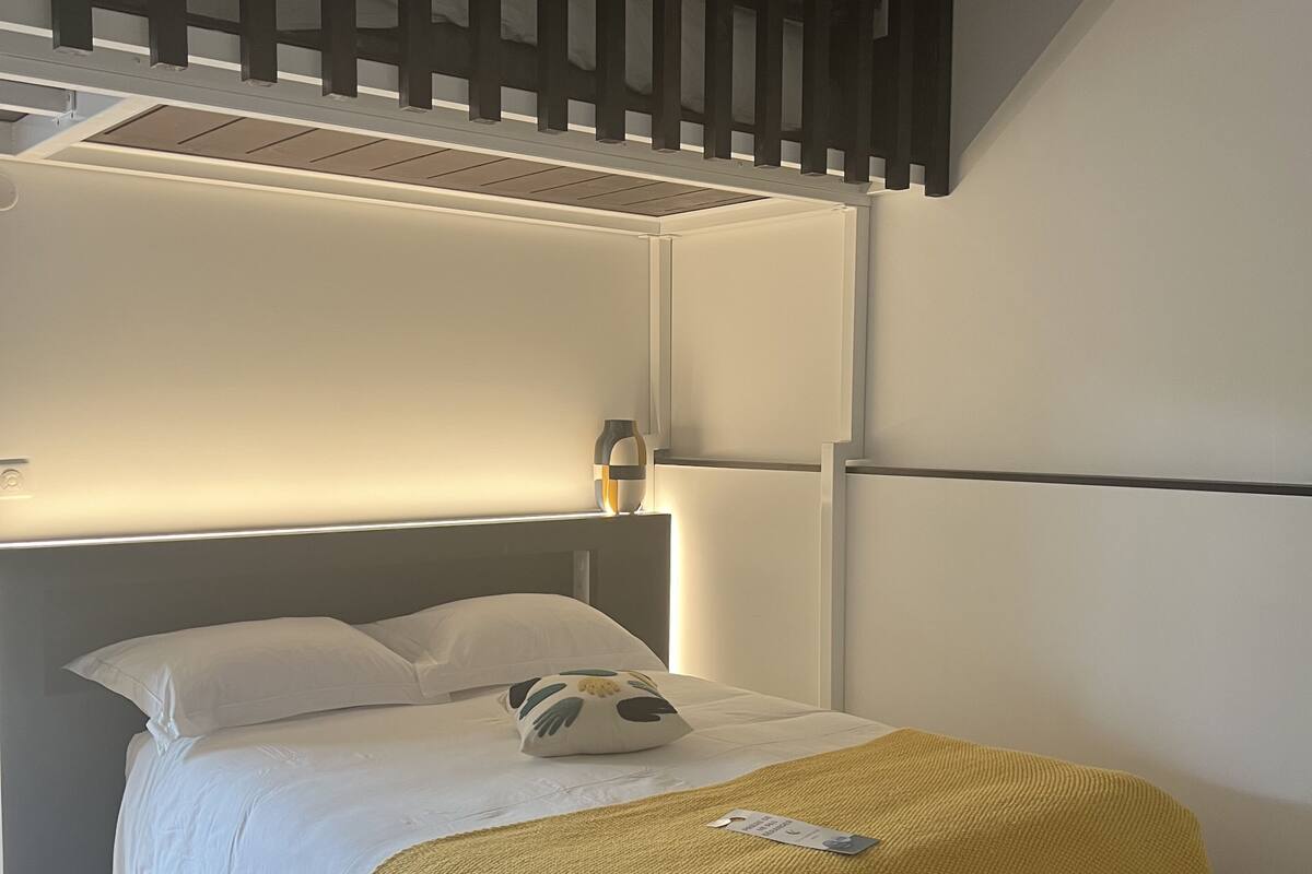 A modern hotel room with a bed, a yellow throw blanket, a pillow, and a headboard with built-in lighting.