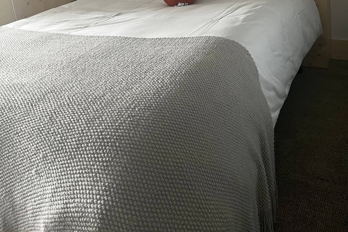 A neatly made bed with a grey textured blanket, white pillows, and a red object on the bed. There are two framed pictures on the wall above the bed.
