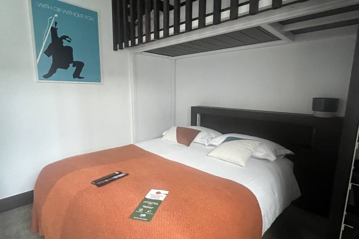 A single bed with an orange throw blanket, a poster on the wall, and a wooden slatted ceiling above.