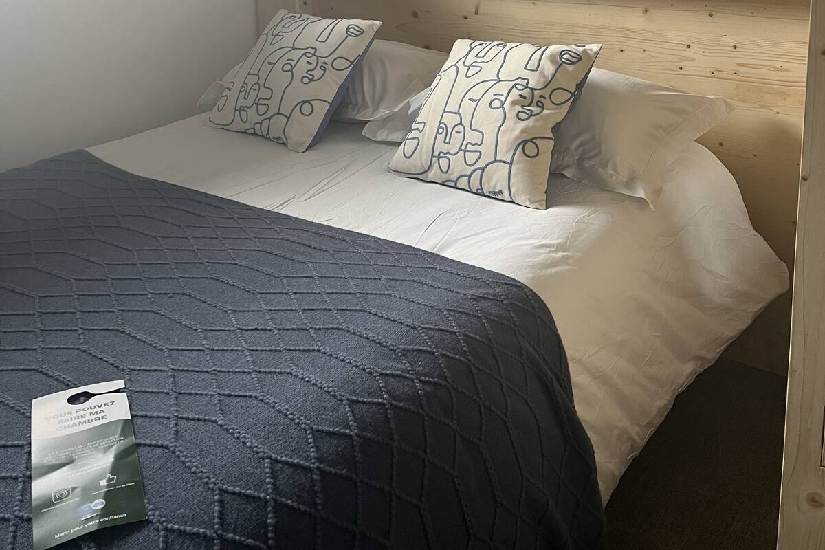 A neatly made bed with patterned pillows, a wooden headboard, and a framed artwork above it.