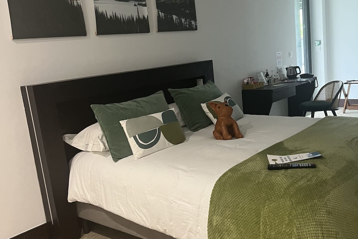 A neatly made bed with green and white bedding, a remote control, and a small decorative item on the bed.