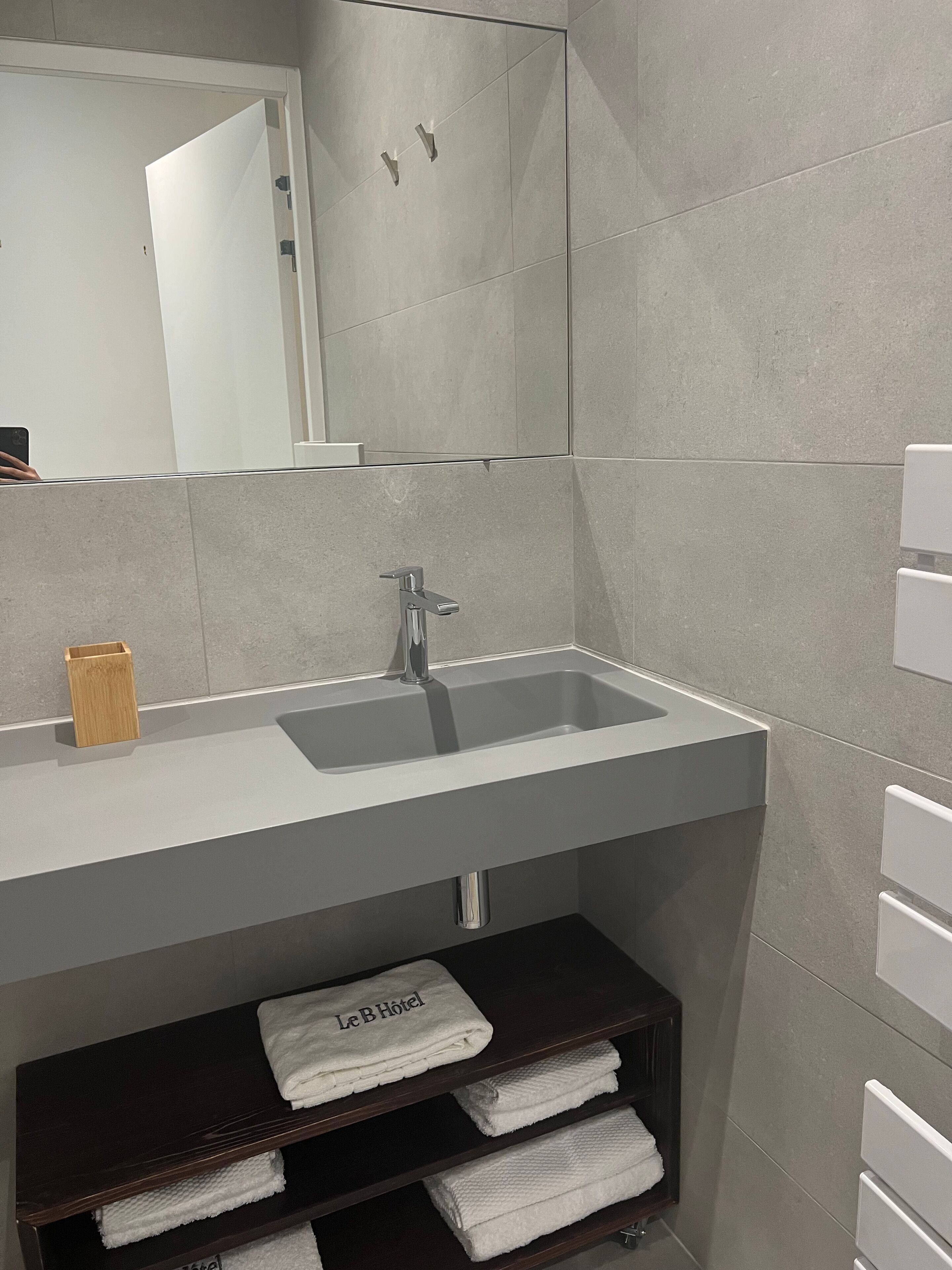 Une salle de bain moderne avec un lavabo blanc, un porte-serviettes en bois et une étagère où sont pliés des serviettes.